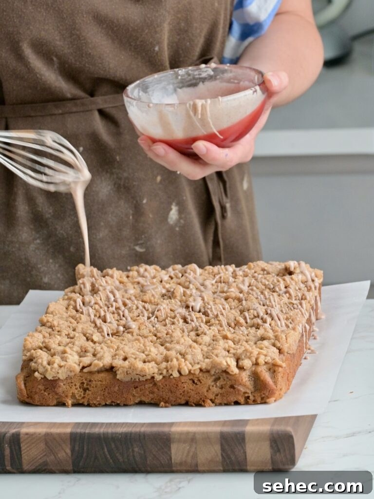 Moist Applesauce Crumb Cake with Cinnamon Streusel 17 Drizzling cinnamon glaze over a freshly baked applesauce crumb cake on a cutting board, showing the thick crumb layer and soft texture.