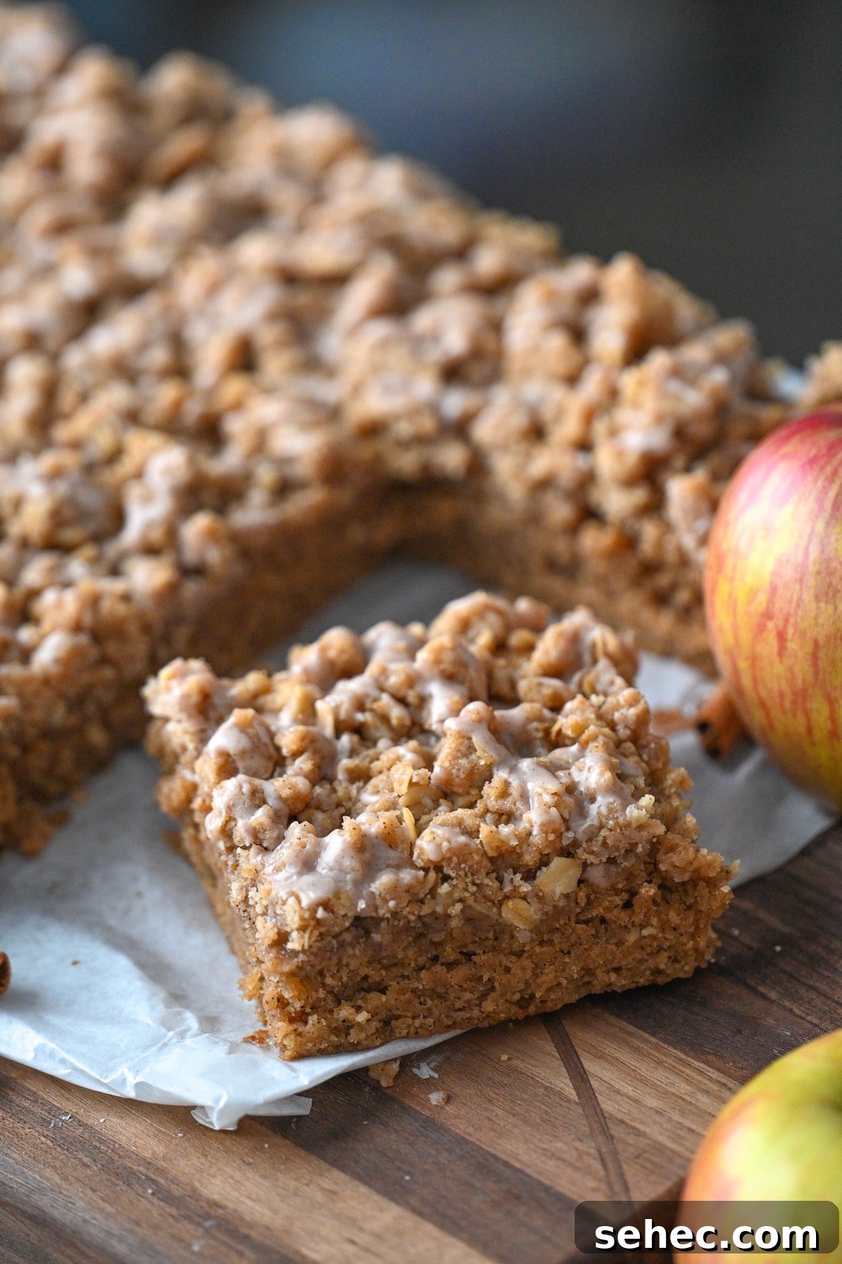 Moist Applesauce Crumb Cake with Cinnamon Streusel 3 sliced piece of homemade applesauce crumb coffee cake on parchment next to fresh apples and the remaining cake.