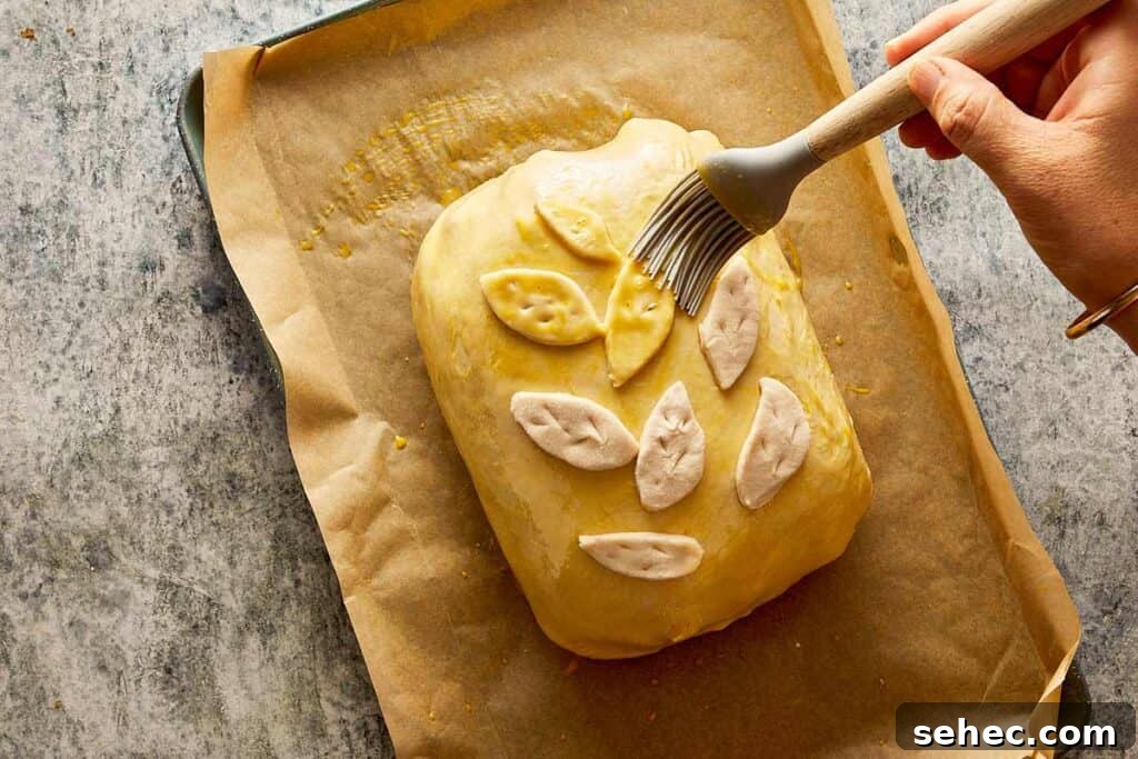 Truffle Beef Wellington Recipe with Red Wine Sauce 14 pastry covered with decorated pastry in the shape of small leaves being brushed with egg to form a layer that will be cooked and used to brown the pastry.
