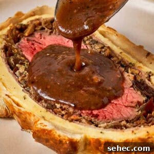 Truffle Beef Wellington Recipe with Red Wine Sauce 20 Beef Wellington slice with sauce being poured using a spoon.