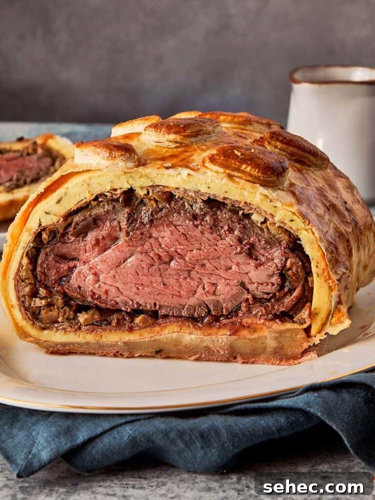 Truffle Beef Wellington Recipe with Red Wine Sauce 4 delicious beef wellington on a plate with cut in half exposing the pink meat inside covered with a delicious pastry