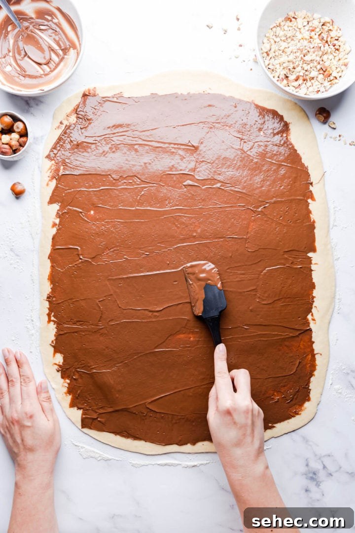 Nutella Babka Recipe: Chocolate-Hazelnut Swirl Loaf 6 top view of a person spreading nutella on top of rolled dough