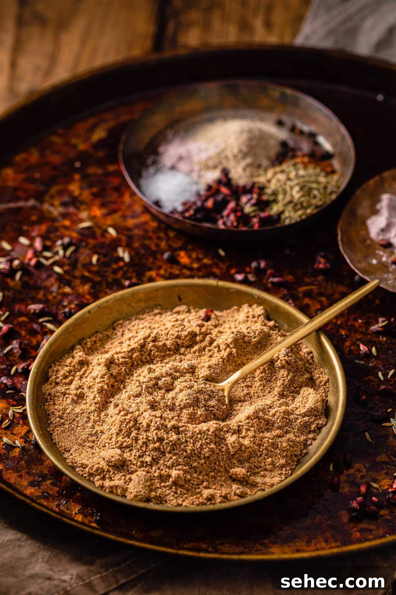 Authentic Chaat Masala Recipe: Homemade Indian Spice Mix 3 Chaat Masala powder in a gold bowl with a small golden spoon with spices in the background