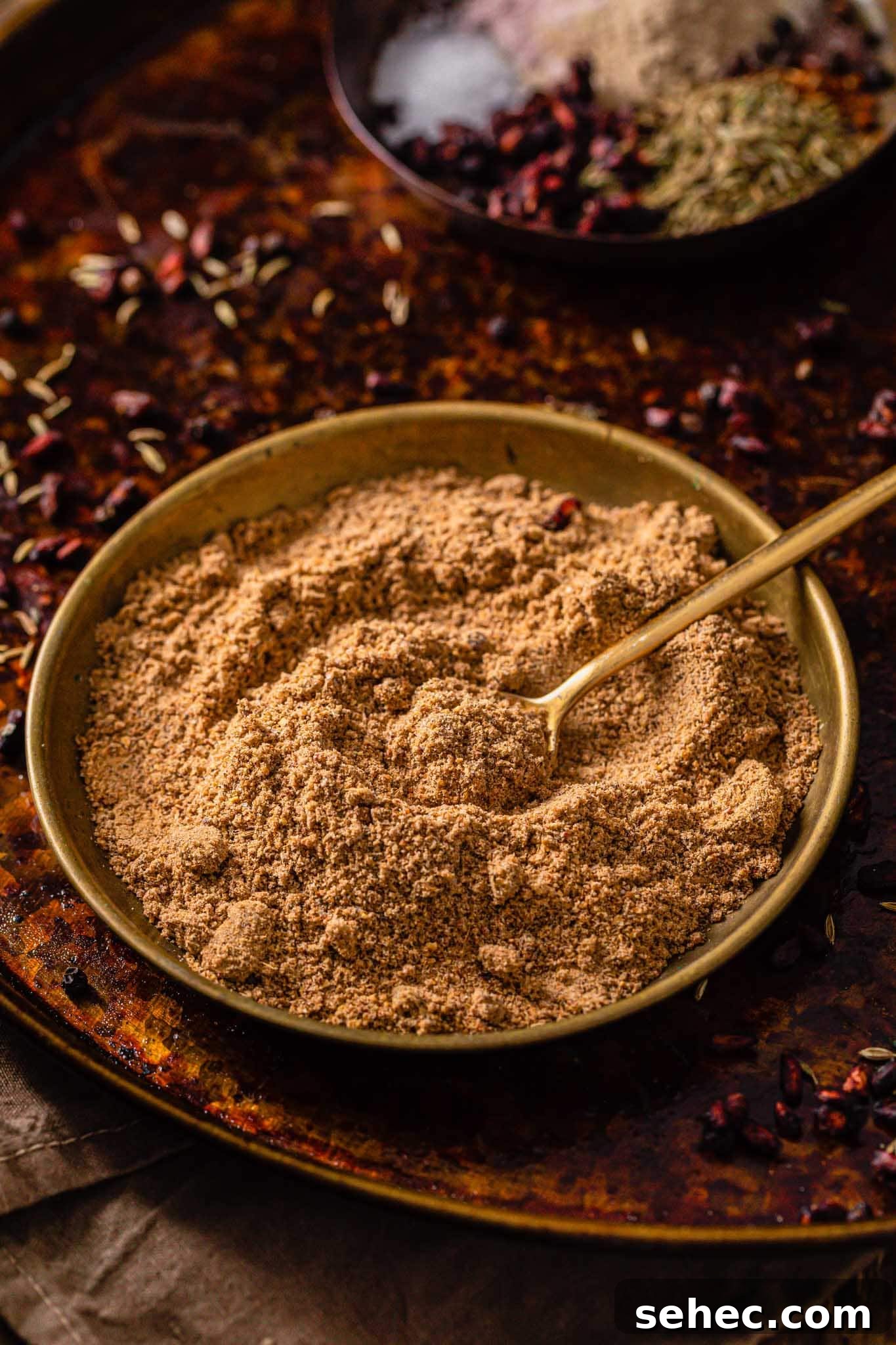 Authentic Chaat Masala Recipe: Homemade Indian Spice Mix 9 Chaat Masala powder in a gold bowl with a golden spoon sitting on a rustic surface
