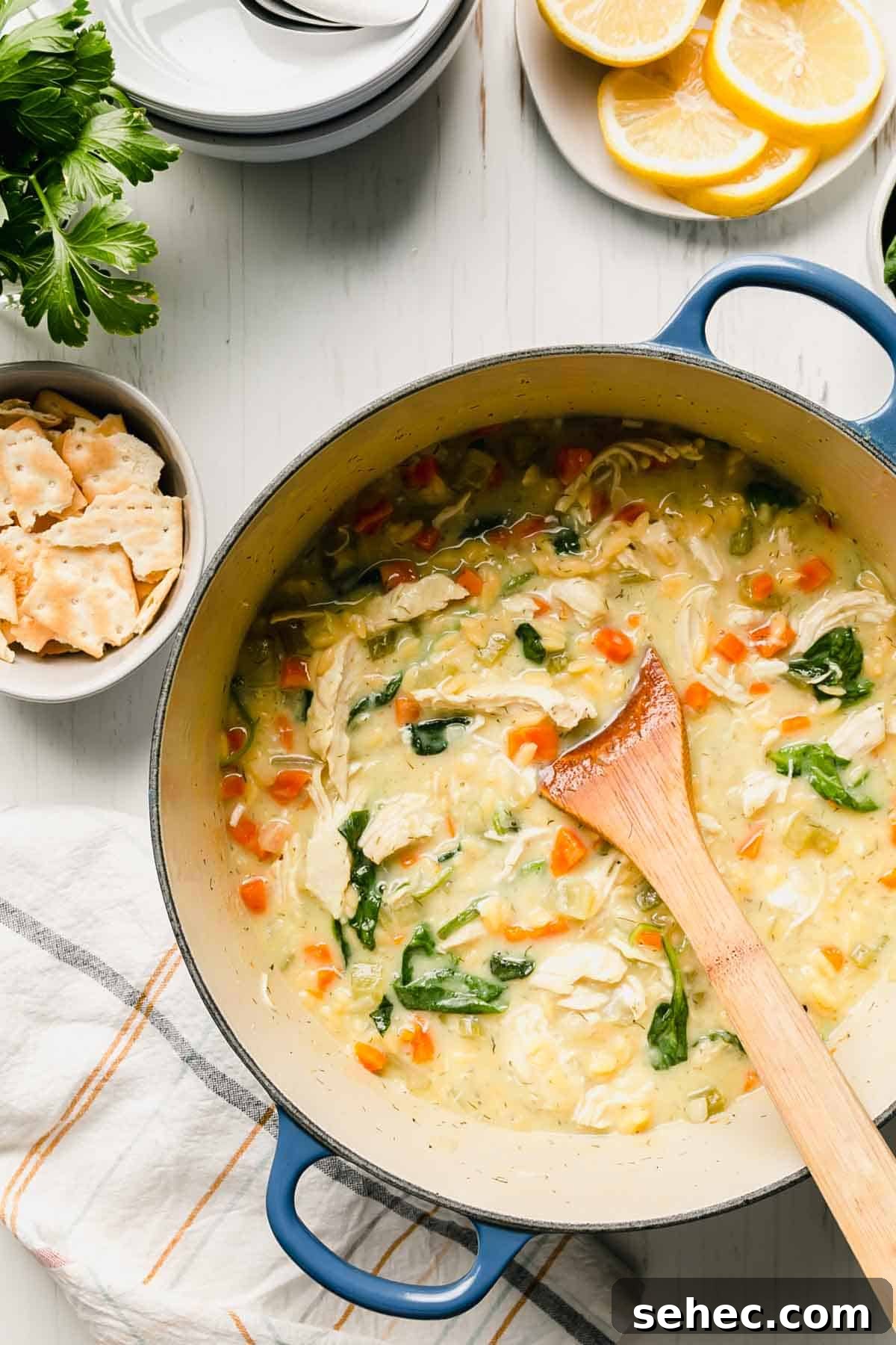 Gluten-Free Lemon Chicken Orzo Soup Recipe 6 A blue pot full of gluten free lemon chicken orzo soup and a wooden spoon.
