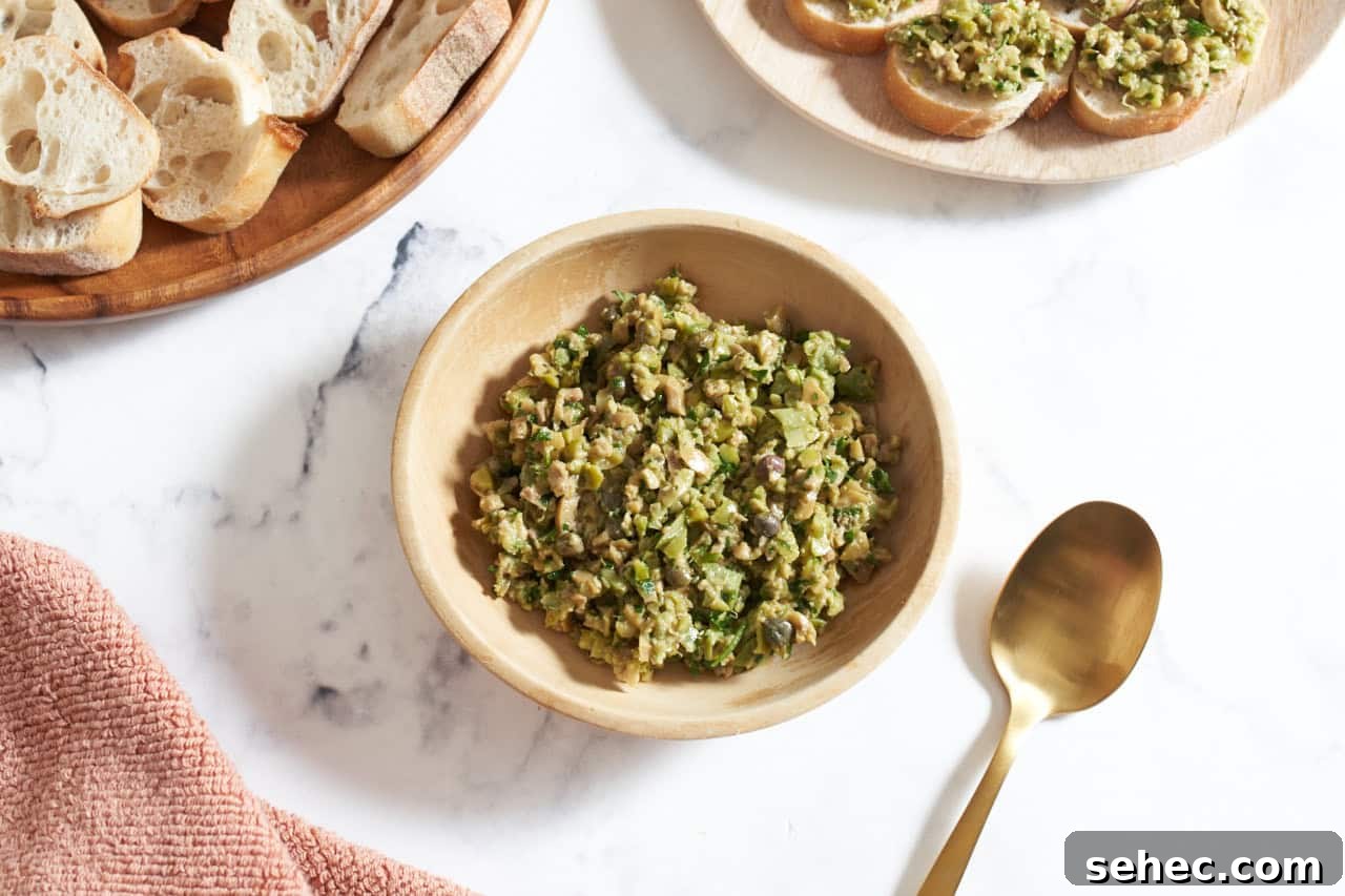 Homemade Green Olive Tapenade Recipe 2 Green olive tapenade in a wooden bowl, a plate of sliced bread is in the upper left, some bread with tapenade on it is in the upper right.