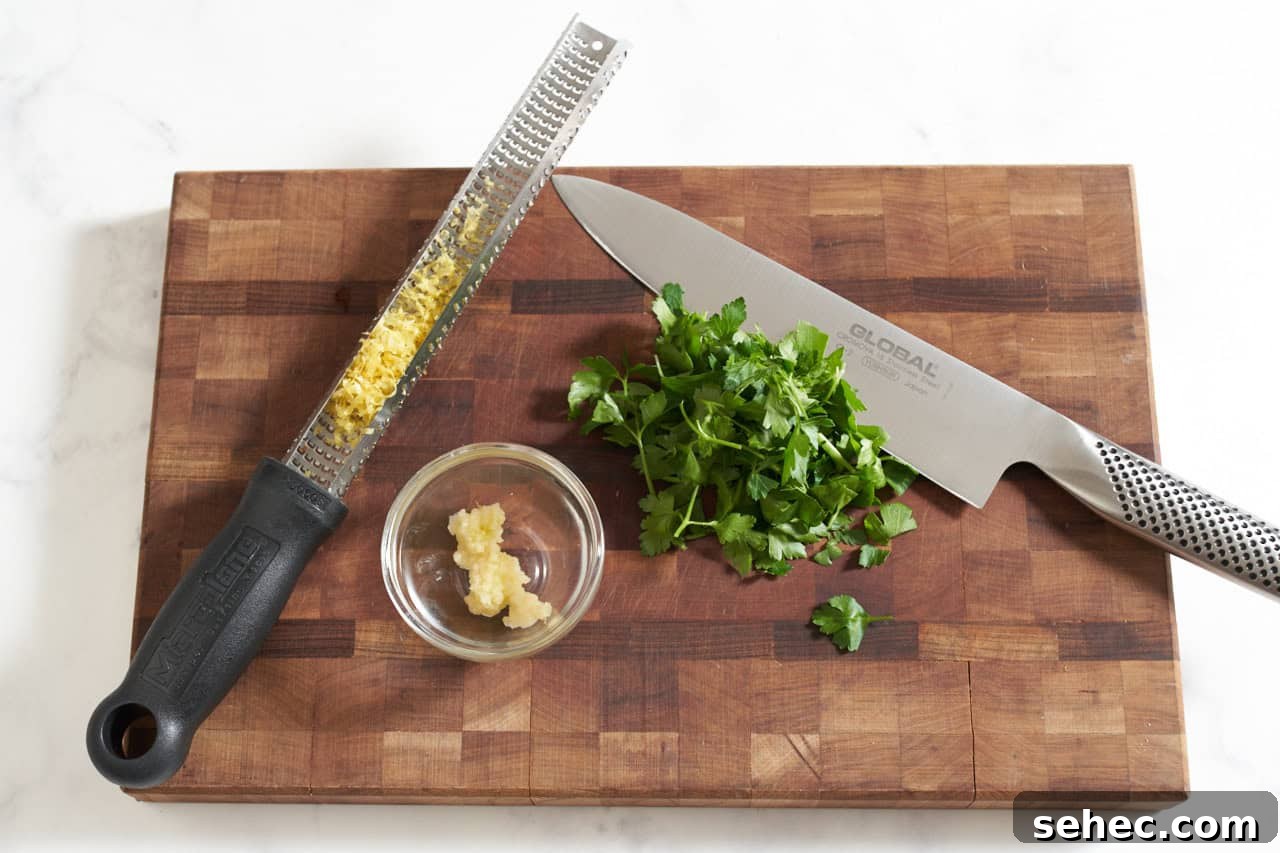 Homemade Green Olive Tapenade Recipe 4 A microplane grater with lemon zest, a chef's knife, some fresh parsley and a bowl of grated garlic on a cutting board.