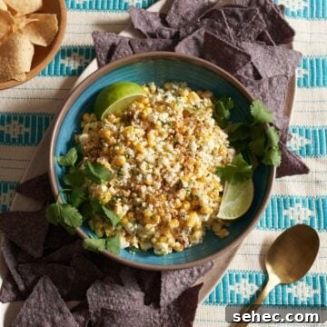 Elote dip in a blue bowl topped with cotija cheese and garnished with lime wedges and fresh cilantro.