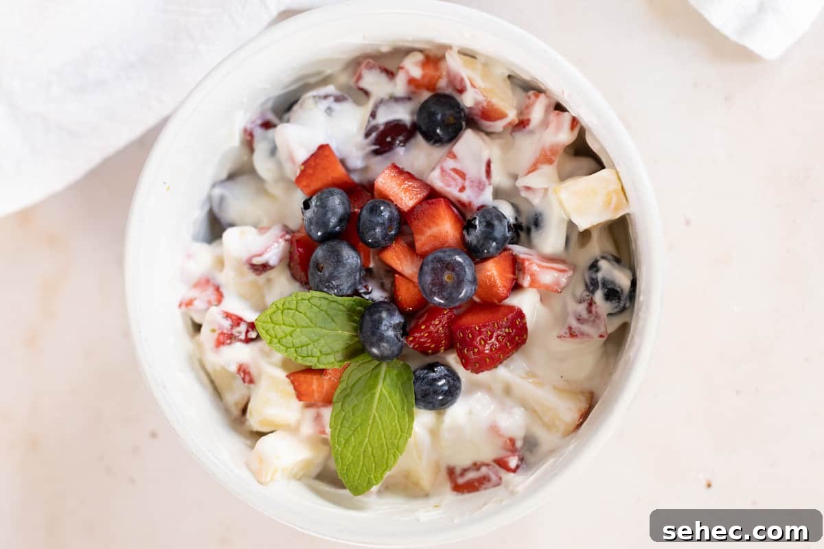 A bowl of creamy fruit salad with mint garnish.