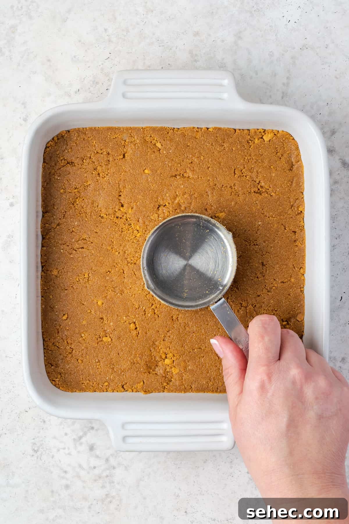 No Bake Strawberry Cheesecake Cups 6 Graham cracker crust being pressed into a square baking pan with a measuring cup.