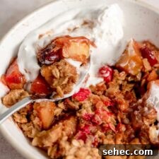 A bowl of cranberry and apple crisp topped with whipped cream with a spoon resting in the bowl.