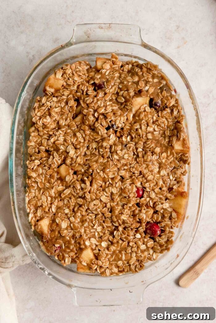 An apple cranberry crumble in a glass oval baking dish before going in the oven.