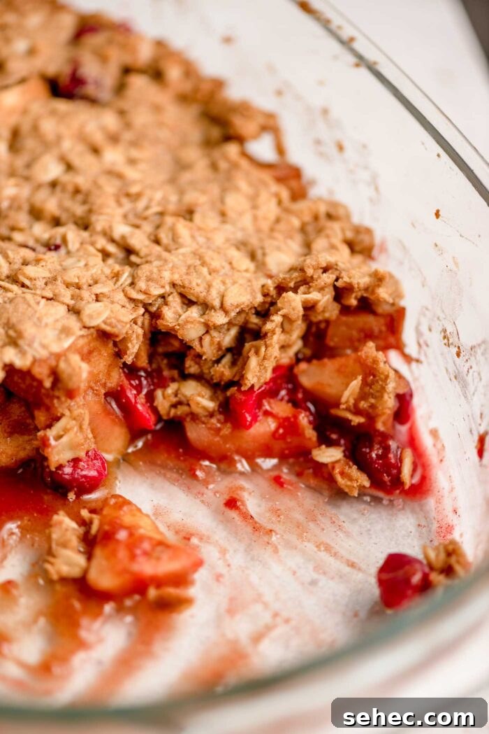 Apple cranberry crisp with a scoop out of it so you can see the apple cranberry filling and oatmeal crumble topping in a baking dish.
