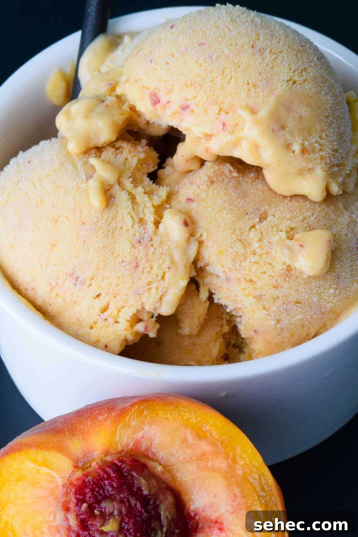 Peach Sherbert in white bowl slightly melted with half peach in front close up view