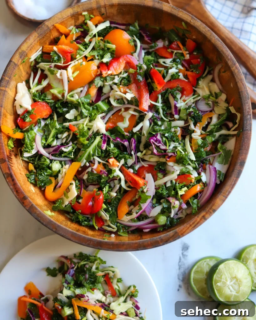 Zesty Crunch Rainbow Slaw Recipe with Colorful Veggies 2 overhead view of a wooden serving bowl with zesty rainbow slaw made with kale, cabbage, onions, peppers, cilantro, lime juice, and more.