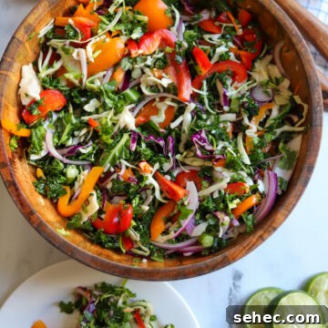 Zesty Crunch Rainbow Slaw Recipe with Colorful Veggies 6 overhead view of a wooden serving bowl with zesty rainbow slaw made with kale, cabbage, onions, peppers, cilantro, lime juice, and more.