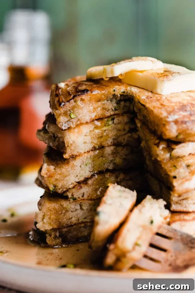 Fluffy Zucchini Bread Pancakes Recipe 2 A stack of sliced open zucchini pancakes with maple syrup dripping down.