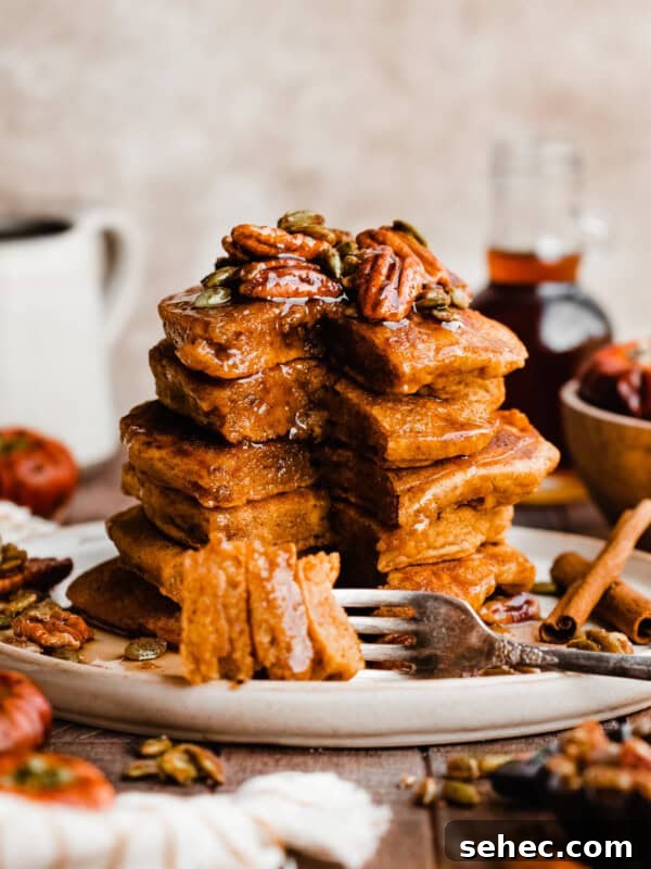 A tall stack of pumpkin pancakes topped with candied pecans and real maple syrup.