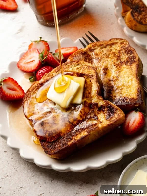 Slices of golden brown brioche french toast on a plate, with butter and maple syrup.