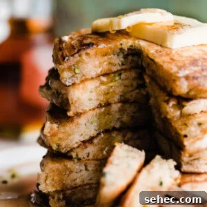 A stack of sliced open zucchini pancakes with maple syrup dripping down.