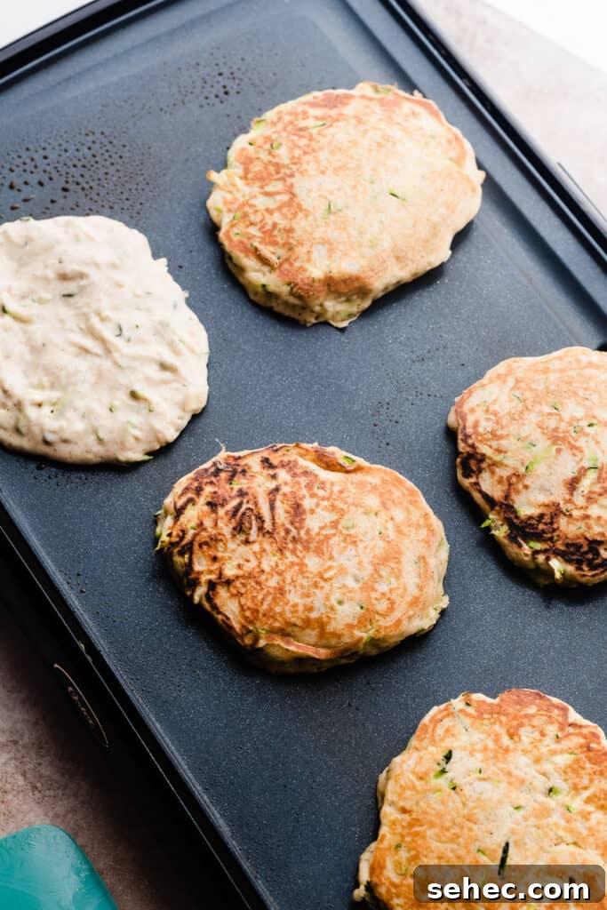 Fluffy Zucchini Bread Pancakes Recipe 7 Zucchini pancakes cooking on a griddle.