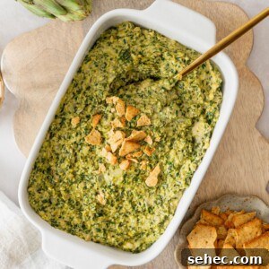 A white casserole dish filled with a vegan spinach artichoke dip with crushed crackers on top.