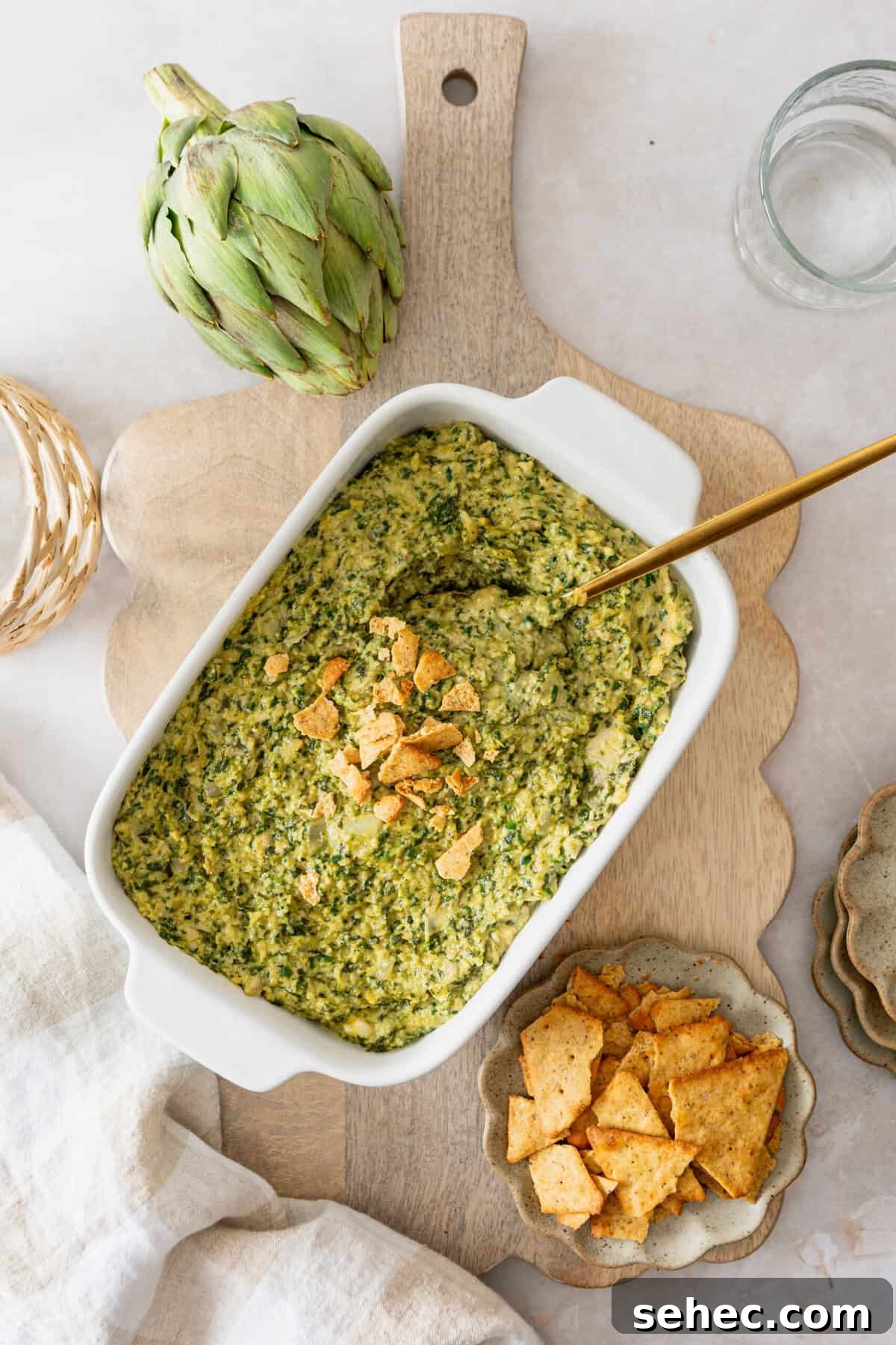 A white casserole dish with a spinach artichoke dip in it topped with crushed crackers.