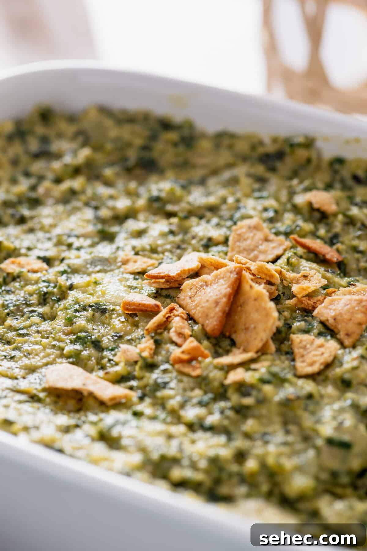 A casserole dish filled with spinach artichoke dip topped with a few crushed crackers.